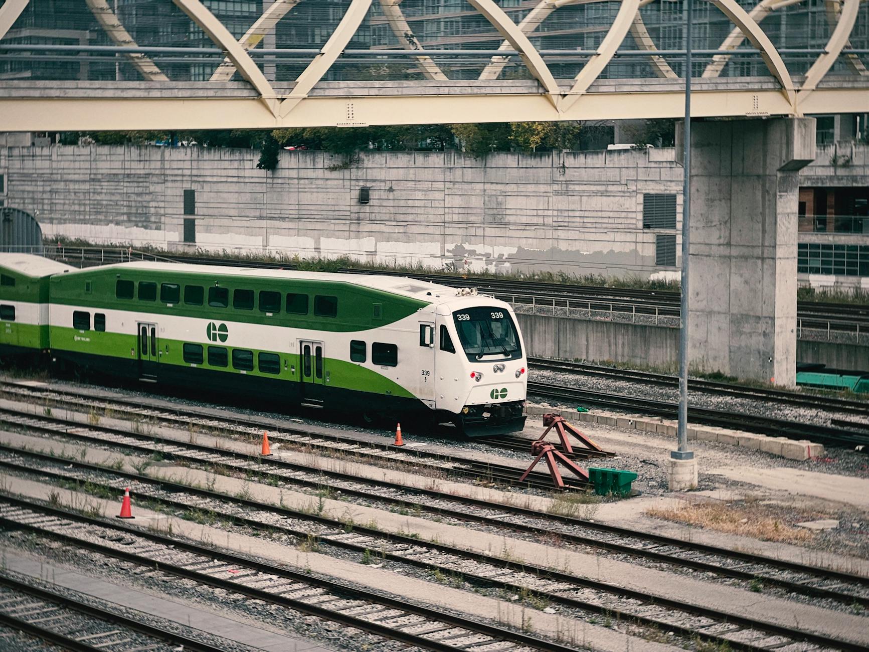 A Go Transit train traveling on urban railway tracks under a bridge.