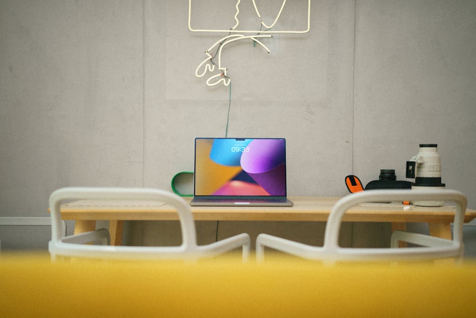 Modern home office with laptop on desk, neon art, and minimalist design.