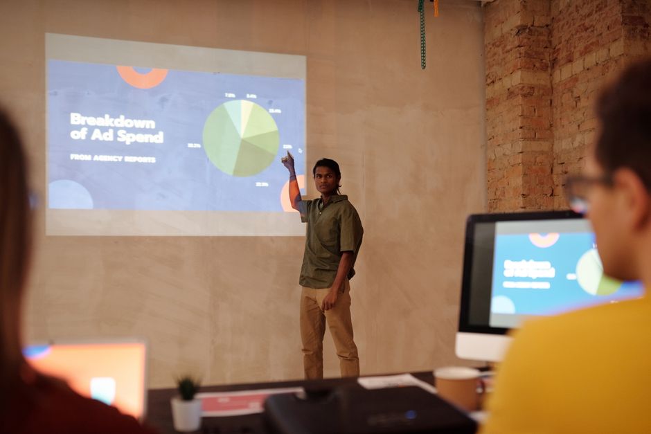 Young man delivering a business presentation on marketing metrics with charts and graphs in a modern office setting.