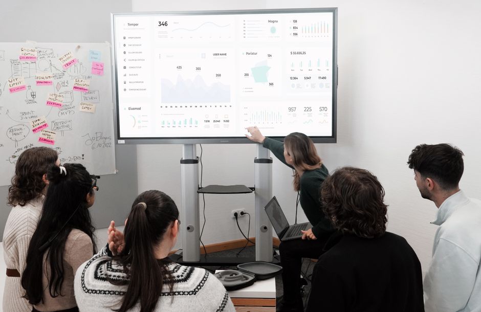 Group of professionals engaged in a business presentation examining charts on a large screen