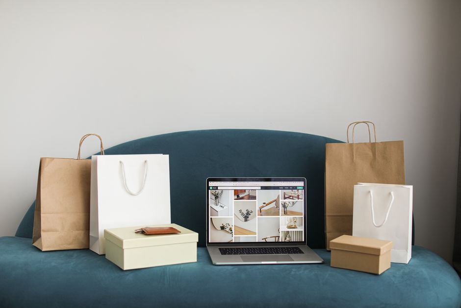 A laptop surrounded by shopping bags and boxes on a blue sofa representing ecommerce and AI conversational shopping