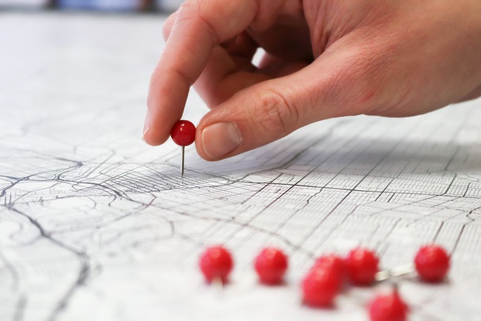 Close-up of a hand placing a red pin on a map indicating geographic location pinning for multi-location local AEO
