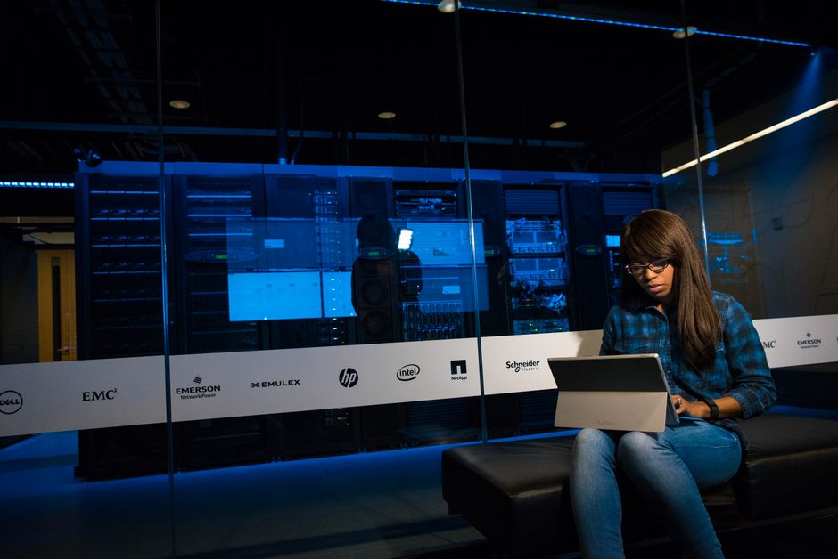 Engineer using a laptop in a server room to inspect AI crawler server logs and verify OAI-SearchBot, ClaudeBot, and PerplexityBot access.